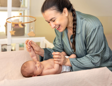 Smiling caregiver holding a newborn’s hands on a changing table during newborn baby care in Dubai