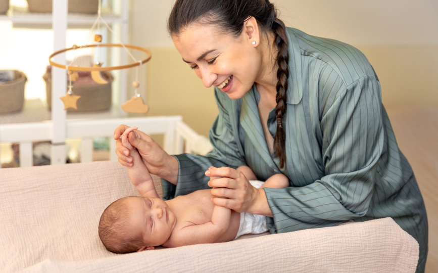 Smiling caregiver holding a newborn’s hands on a changing table during newborn baby care in Dubai