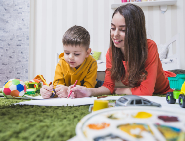 Caregiver drawing with a young boy on a green rug during after-school baby care in Dubai
