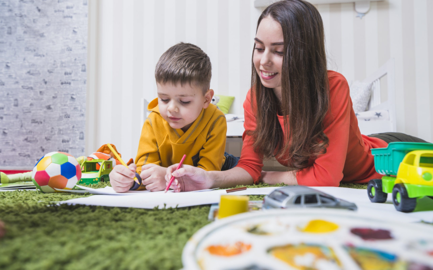 Caregiver drawing with a young boy on a green rug during after-school baby care in Dubai